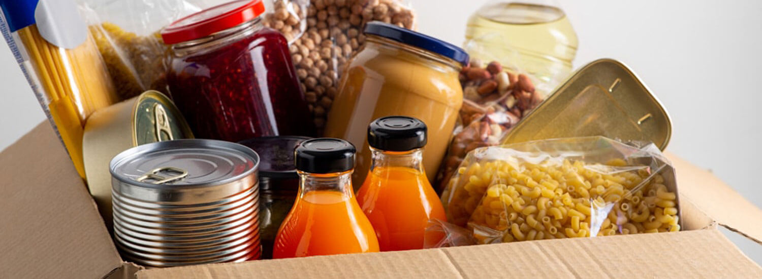 Food items (including dry pasta, canned goods, and jarred spreads) in cardboard box.