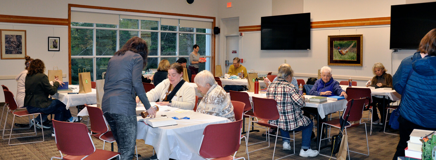 2024 Book Bonanza Fourteen adults sit at tables, working on crafts.