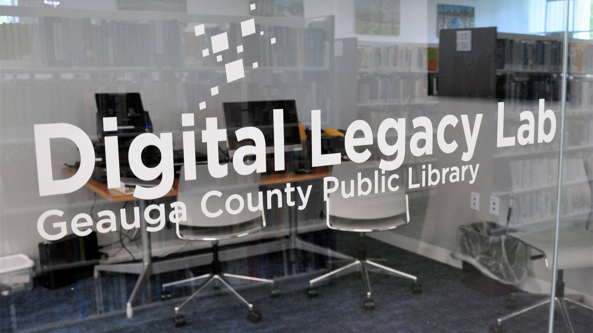 Digital Legacy Lab at Bainbridge Branch Glass wall labeled "Digital Legacy Lab" in a library study room with computers and chairs inside.