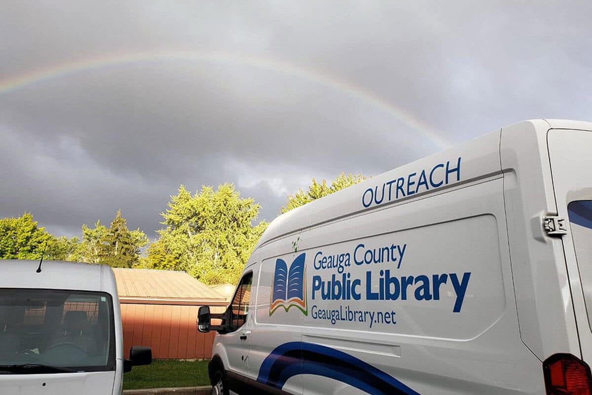 A library outreach van under a cloudy sky with a rainbow.